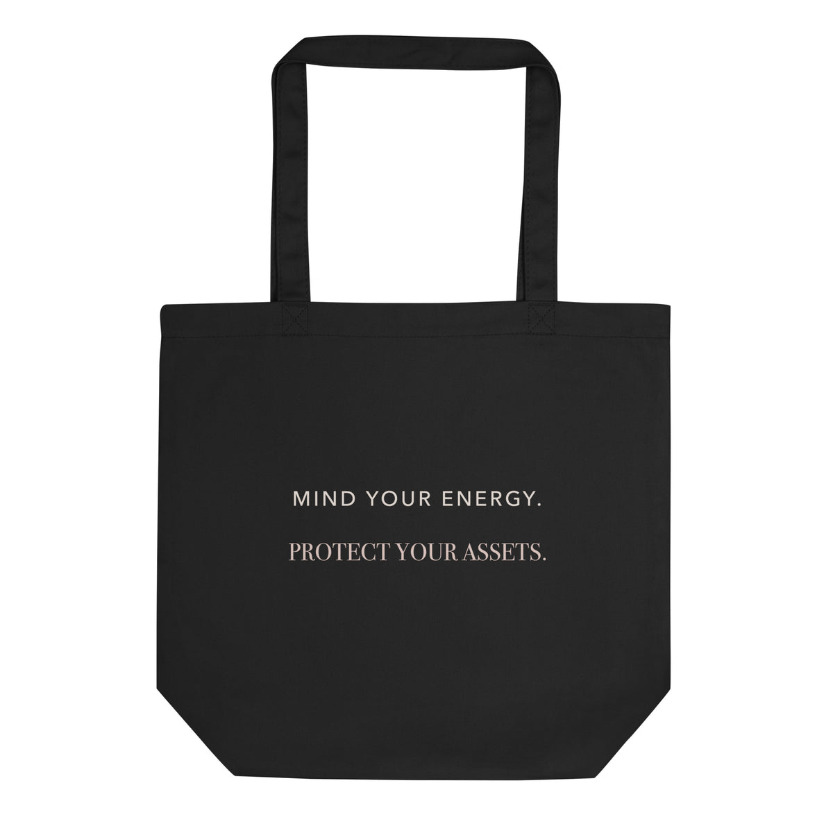 Black organic-cotton tote reading ‘Mind Your Energy. Protect Your Assets.’ in ivory and rosy-champagne typography.