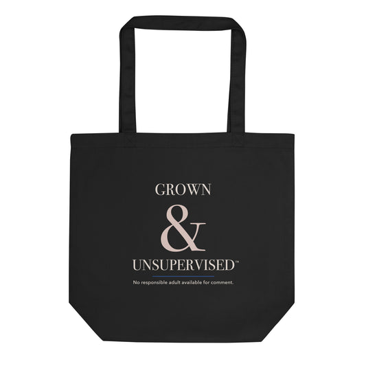 Black organic-cotton tote reading “Grown & Unsupervised™” in ivory, rosy-champagne, and royal-blue typography.