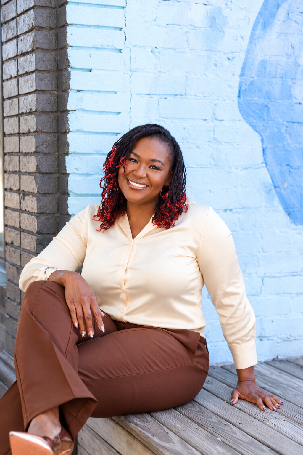 Dr. Shermnae D. Jones, founder of Voluptuocity, seated against a pale-blue brick wall
