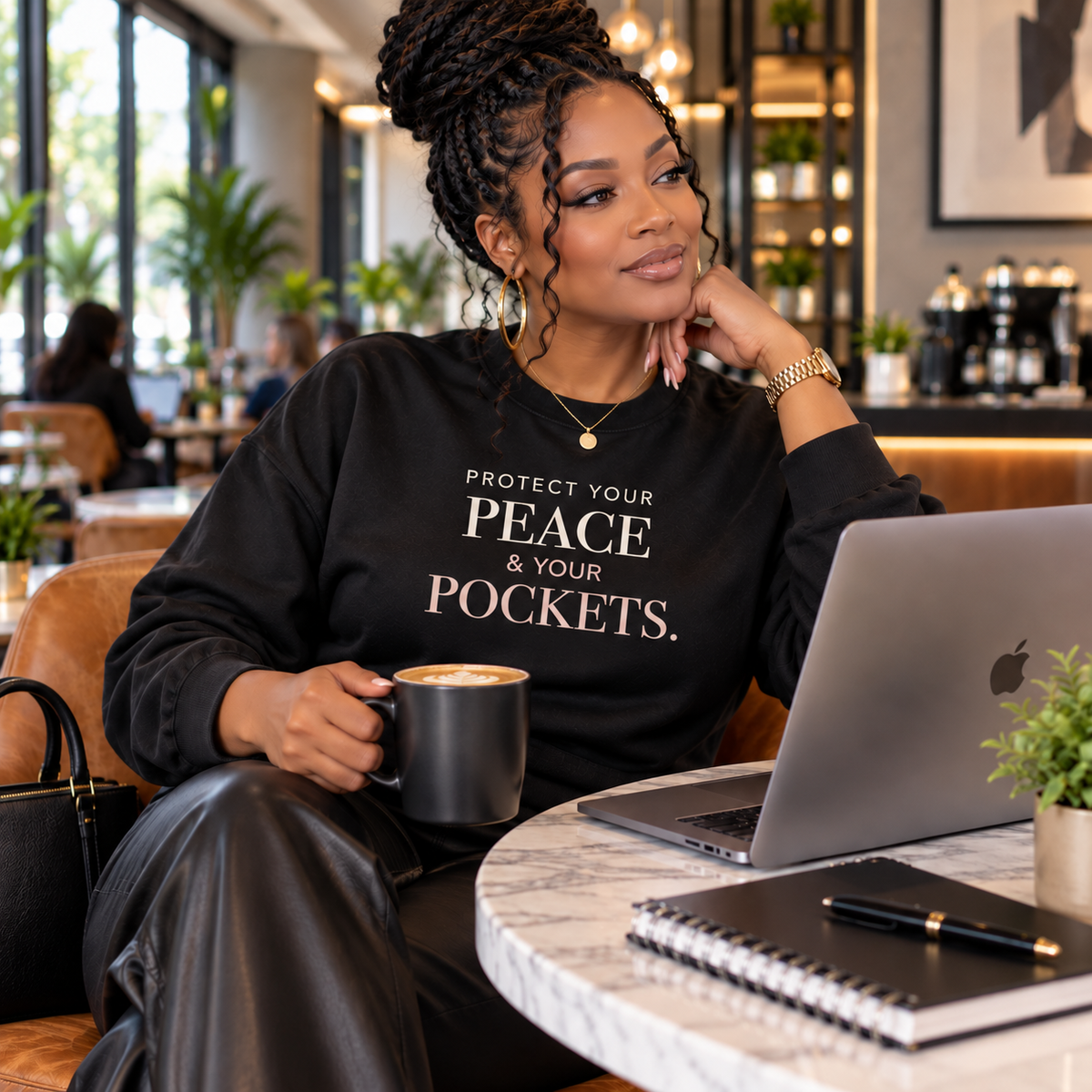 Woman wearing the black Voluptuocity™ Protect Your Peace & Your Pockets crewneck sweatshirt in an upscale coffee shop.